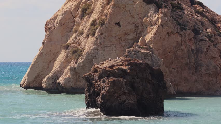 Dramatic rock formations rise from turquoise ocean waves under a bright sunny sky.