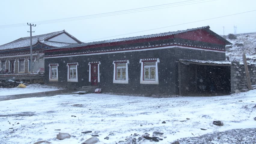 Traditional Tibetan stone houses in a remote mountain village during a light snowfall