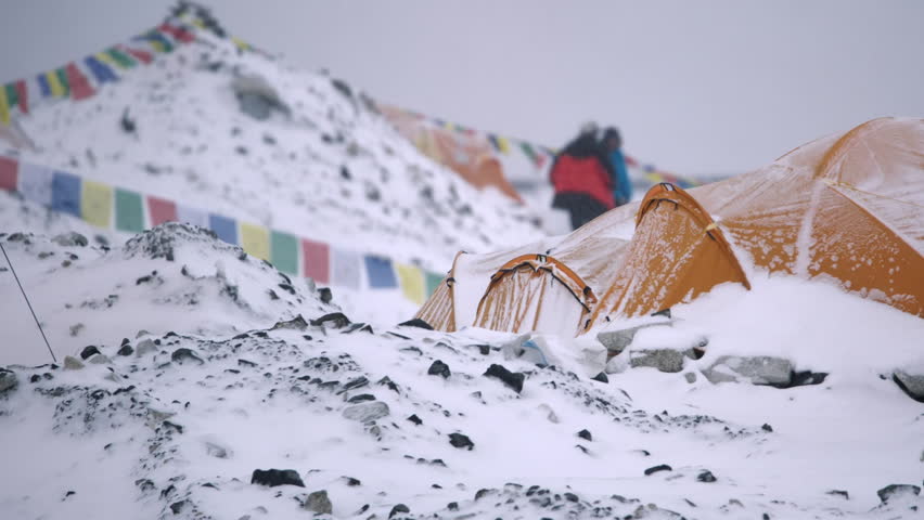 Tents and climbers at a snowy high altitude base camp with colorful Tibetan prayer flags