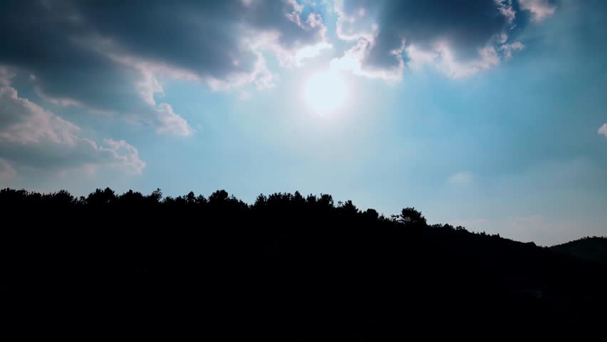 Sunlight Shining Through Clouds Above A Dark Forest Silhouette At Sunset