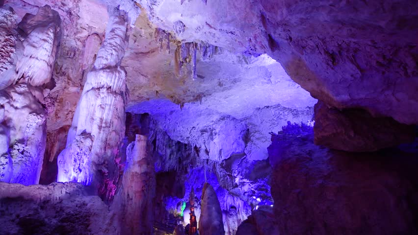 Stalactite formations illuminated by colorful lights inside a deep underground limestone cavern system