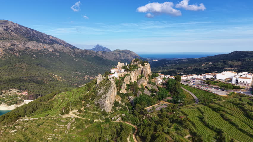 Guadalest castle perched on rocky hilltop in Alicante Spain surrounded by green mountains valleys and Mediterranean sea visible in background