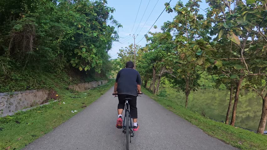 Man Cycling on Road Beside Lake