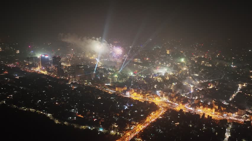 Night aerial view of Hanoi skyline and fireworks near Hoan Kiem Lake with illuminated bridge and atmospheric city haze.