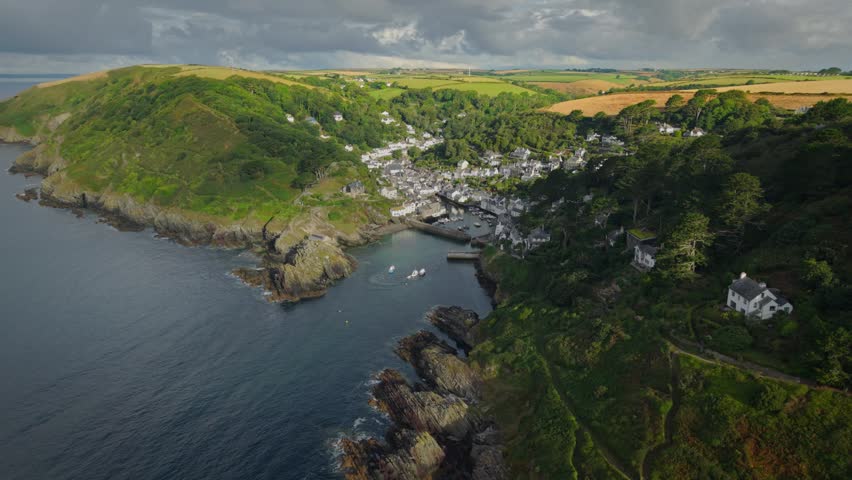 Aerial view of the historic fishing village of Polperro nestled between steep green cliffs and the rocky coastline with boats in the harbor Polperro, England, United Kingdom.