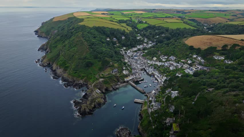 Aerial view of the historic fishing village of Polperro with its harbor, white houses, and green hills in Polperro, England, United Kingdom.