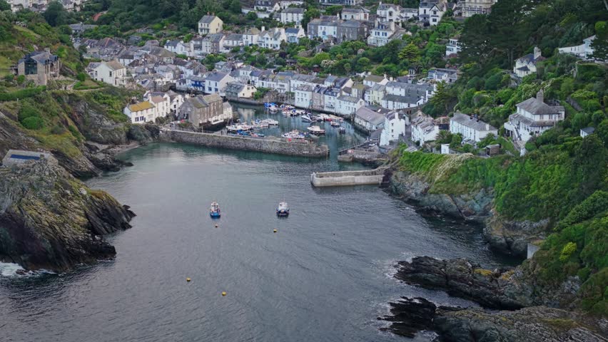 Aerial view of the historic fishing village of Polperro with its harbor, white cottages, and lush green hillsides in Polperro, England, United Kingdom.