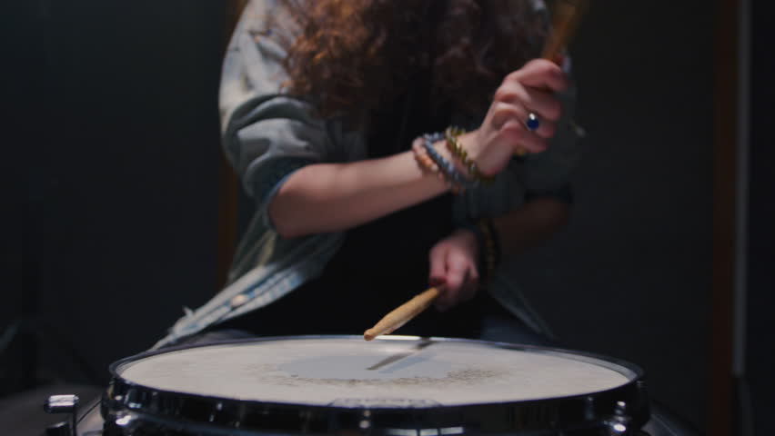 Young female drummer passionately playing a drum kit in a professional rehearsal studio, energetically striking cymbals and drums with drumsticks. Hair flying. Rock Feminist style. Woman power.