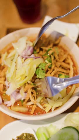 Close-up overhead shot of hands using a spoon and fork to mix spicy curry noodles