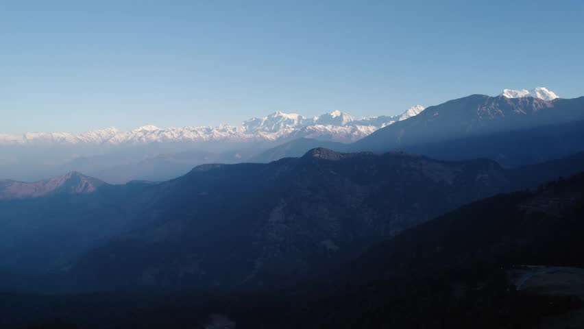 Aerial view of the snow-capped Himalayan peaks of Chopta Tungnath under a clear blue sky with shadowed mountain ridges in the foreground, Chopta, Uttarakhand, India.