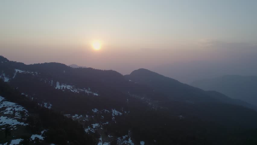 Aerial view of Chopta Tungnath with snow-capped mountain ridges and hazy sunset sky in Chopta, Uttarakhand, India.