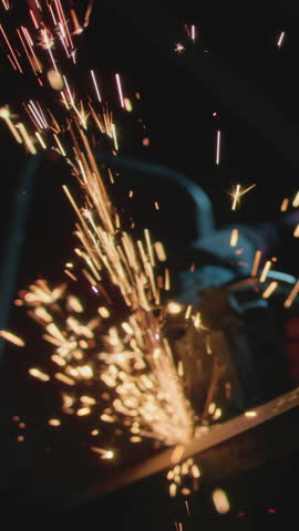 Male industrial or construction worker cuts metal with a angle grinder. Man uses circular saw at garage or workplace. Cutting raw material with flying red sparks at the factory or plant. Slow motion