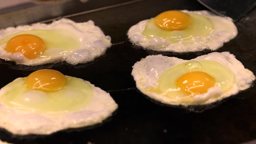 Egg cracking process above hot metal pan cooking closeup