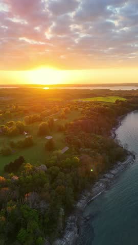 Aerial view of the sunset over the coastline of Bockholmwik with green fields and lush trees in Munkbrarup, Schleswig-Holstein, Germany.