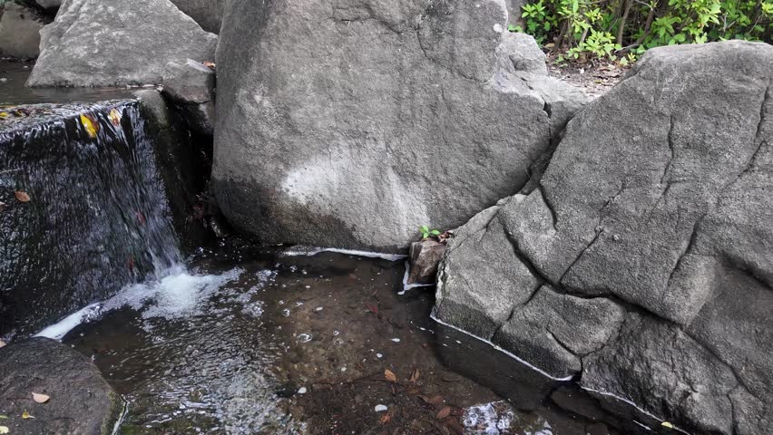 Close-up of clear water flowing down from large rocks, a babbling brook and a small waterfall in a park
