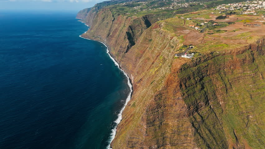 Rugged Atlantic coastline of Madeira Island with Ponta do Pargo lighthouse perched on high cliffs, drone shot