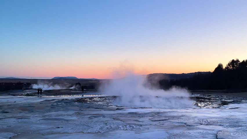 Steam can be seen rising from dark rocks in Iceland. The clouds above create a backdrop as the natural features showcase the unique terrain and volcanic activity in the area.