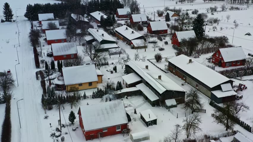 Small village with snow covered trees and houses in aerial view on gloomy winter day