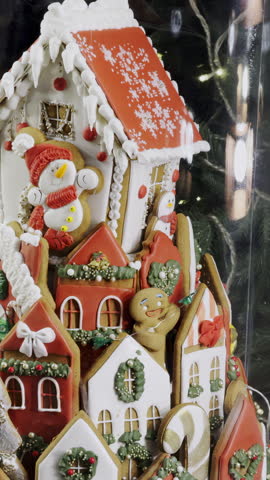 Decorative gingerbread house stands in festive holiday display behind glass. Icing details and candy shapes create cheerful Christmas vibe