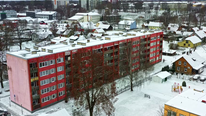 Cold winter cityscape showing a red residential building and snowy rooftops from an aerial view