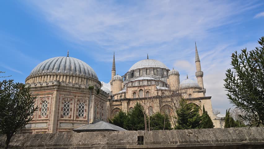 Historic Ottoman imperial mosque in Istanbul, Turkey. Beautiful ancient architecture with domes and minarets against a blue sky with clouds