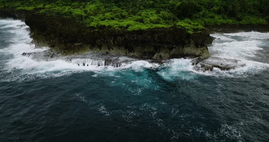 Coastal cliff with waves washing over reef and foamy ocean surface. Siargao, Philippines.