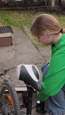 Vertical video. Brother and sister inflating bicycle tire with pump in backyard