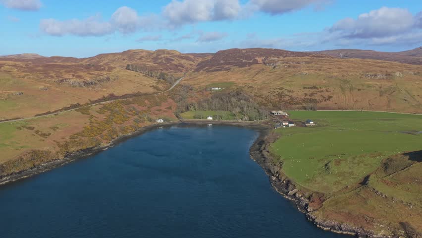 Beautiful aerial footage of a secluded bay with blue water surrounded by rolling hills and green pastures on a sunny day in scotland