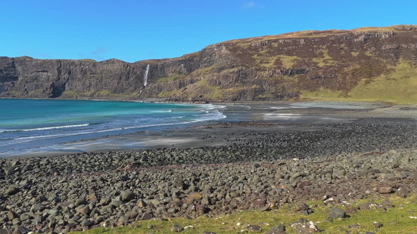 Majestic view of talisker bay beach on the isle of skye, scotland. Turquoise waves lapping on the rocky shore with a waterfall cascading down cliffs
