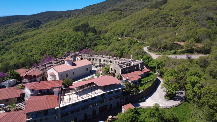 Wide angle aerial view of Panagia Varnakova Monastery on a mountain summit with stone cells and endless forest, reflecting spirituality and heritage tourism in Greece, Europe.