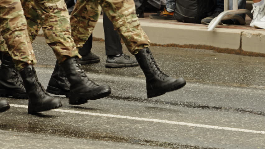 Close-up view of synchronized military boots and camouflage trousers marching in tight formation on wet asphalt during a disciplined parade, emphasizing unity, precision, and coordinated movement.