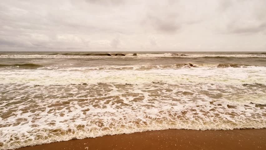 Rough Muddy Sea Water Waves Crashing on Sandy Beach Under Cloudy Sky. Dirty Muddy Sea Water Crashing on Coastline After Monsoon Rain Storm.
