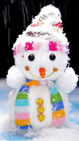 Festive little snowman toy wearing a colorful striped knitted hat and scarf standing as white winter snow falls heavily around it