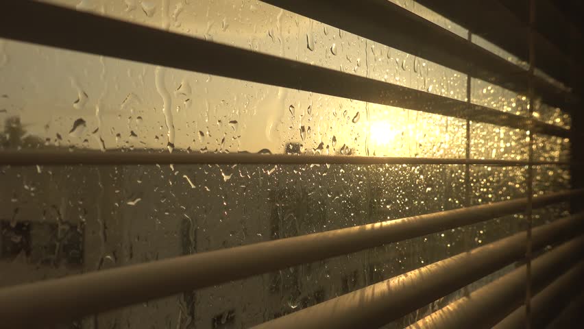 Stockholm, Sweden Hard rain falls on a window with blinds and a setting sun.  