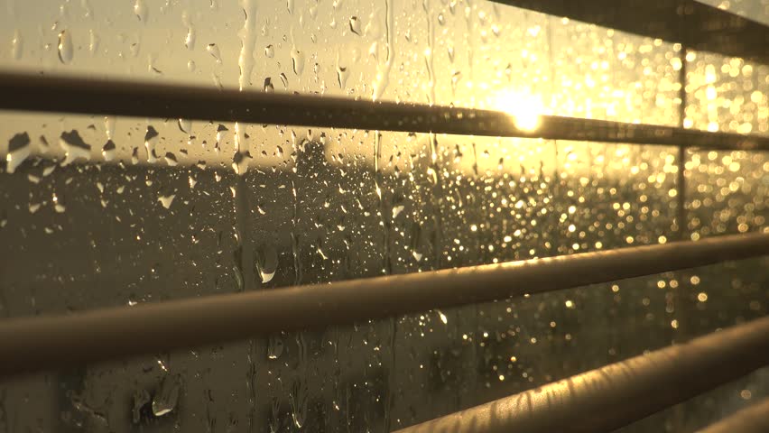 Stockholm, Sweden Hard rain falls on a window with blinds and a setting sun.  