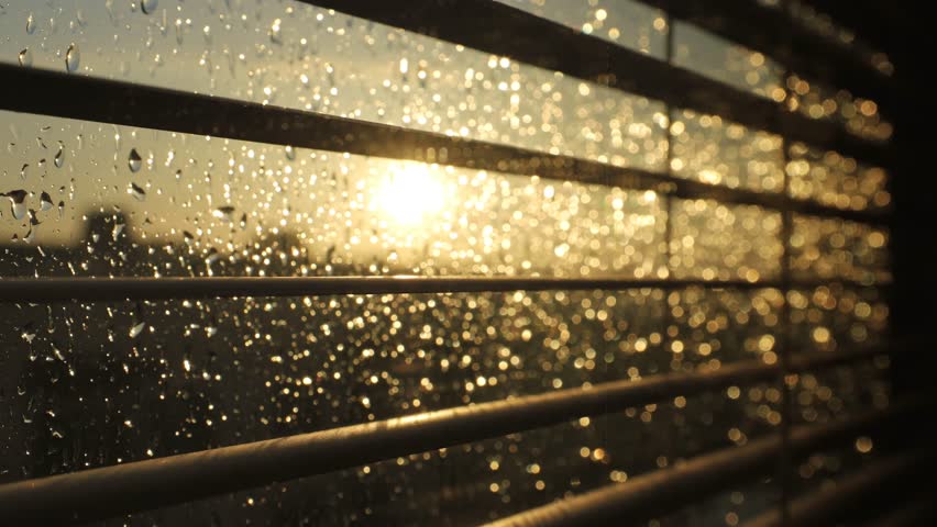 Stockholm, Sweden Hard rain falls on a window with blinds and a setting sun.  