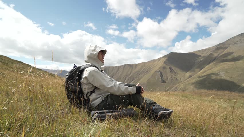 4K traveler relaxing on a mountain meadow enjoying peaceful nature and scenic landscape.