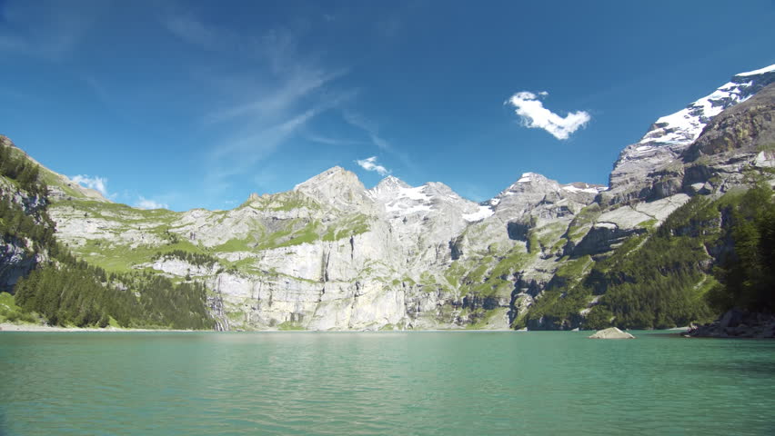 Mountain lake with a rock in the foreground, surrounded by forested slopes and snow-capped peaks