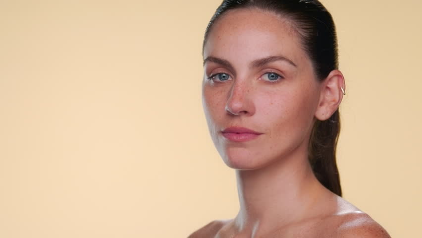 Headshot of fair-skinned freckled brunette Latina looks over her shoulder, smiling, and turning body out of the camera walks away on tan backdrop | pure skin commercial