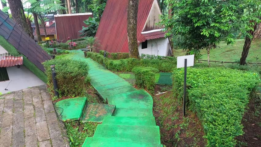 Green concrete pathway and stairs among wooden A-frame cabins in pine forest