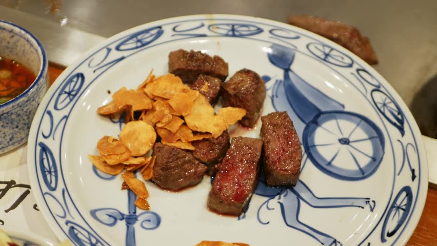 pov to a plate full of Kobe steak grilled cutted with golden fried garlic plate ready to eat in Japanese style, japanese kobe steak cooking. wagyu kobe beef steak on teppanyaki style