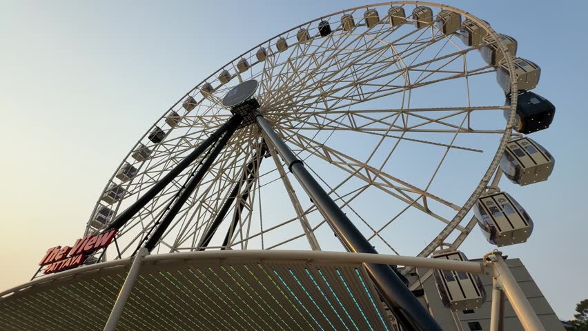 Low angle tracking shot of a giant white Ferris wheel structure named The View Pattaya against a clear blue sky