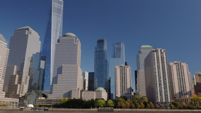 Lower Manhattan skyline with One World Trade Center and modern skyscrapers on sunny day, New York City waterfront view, USA.