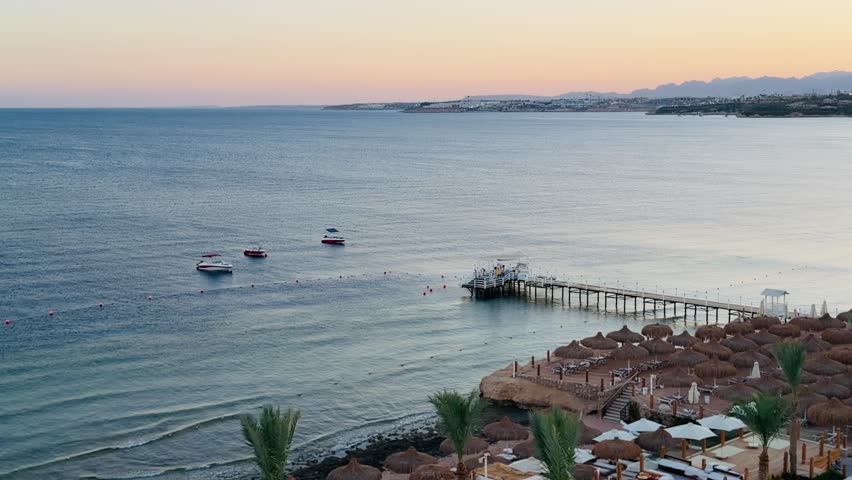 Beautiful Red Sea coast at sunset in Sharm El Sheikh, Egypt. Scenic view of luxury hotel beach with umbrellas, pier, and boats. 5-star all inclusive resort holiday summer travel concept.