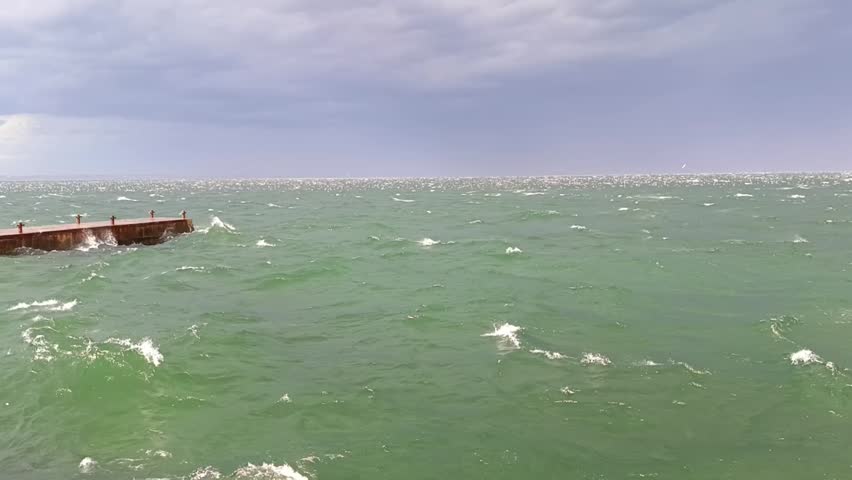 Stormy sea with rough green water and white waves under cloudy sky. Windy coastal weather, ocean surface, natural marine background.