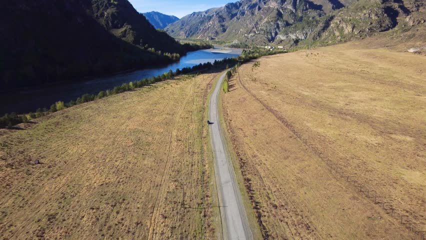 Aerial Road Through Valley With Car, Golden Meadow, Distant Lake And Craggy Mountains Solo Driver On Reflective Road Trip, Landscape Photographer Framing Shots, Nature Observer Pausing At Overlook