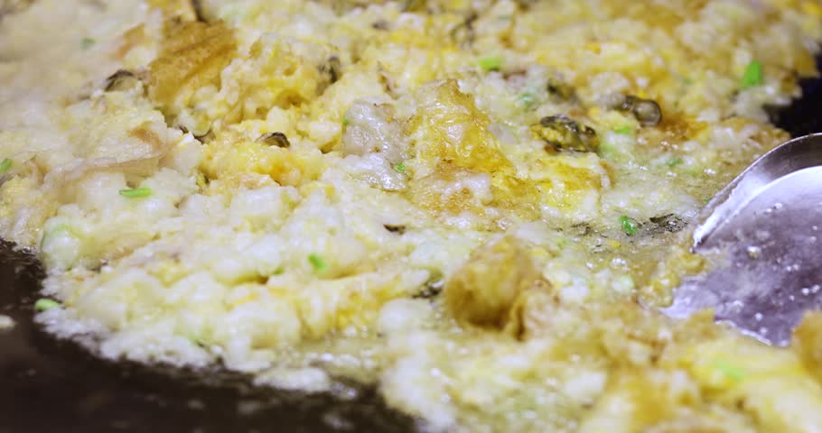 Oyster omelet cooking on a hot pan with metal spatulas. Delicious street food, live cooking, and tasty seafood meal preparation, close-up