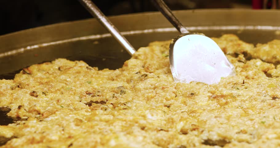 Oyster omelet cooking on a hot pan with metal spatulas. Delicious street food, live cooking, and tasty seafood meal preparation, close-up