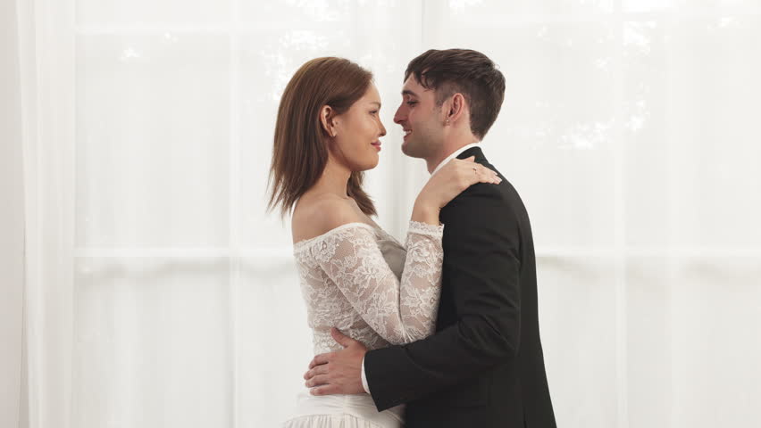Bride and groom share a tender embrace, smiling forehead to forehead in a soft, romantic wedding portrait.
