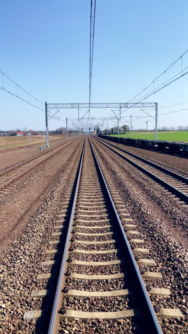 Rear view from a moving train. Train tracks disappearing on the horizon. Passing a train station platform